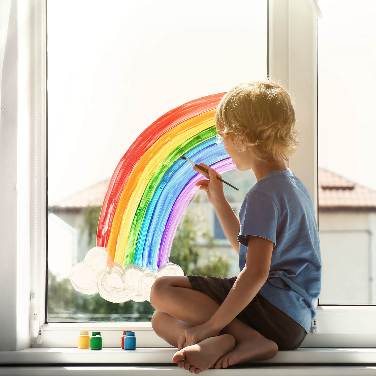 Ein Kind, sitzend auf der Fensterbank, malt einen Regenbogen an die Scheibe eines Fensters. Mit dem Link öffnet sich eine größere Ansicht.